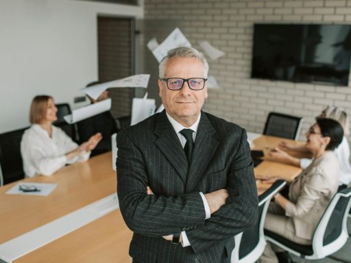 Business executive standing confidently in meeting room with team engaged in discussion behind.