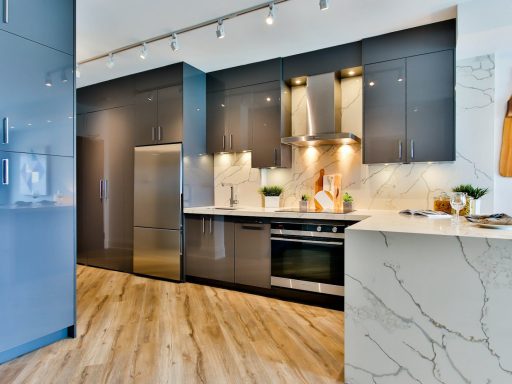 Modern kitchen with grey cabinets, marble countertops, and light wood flooring